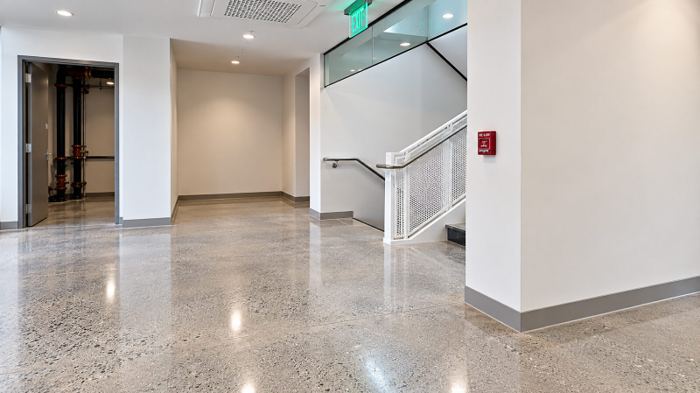 Stair hall with polished concrete flooring running tight to the wall base and around a glass-railed stair enclosure