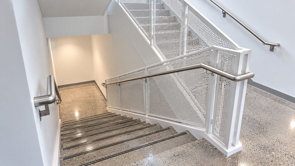 Polished concrete stair landing viewed from above, with perforated metal guardrails and dark abrasive nosing strips recessed into each tread
