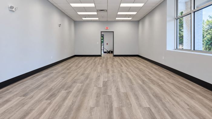 Back-of-house retail room with the same wood-look plank flooring continuing through an open doorway