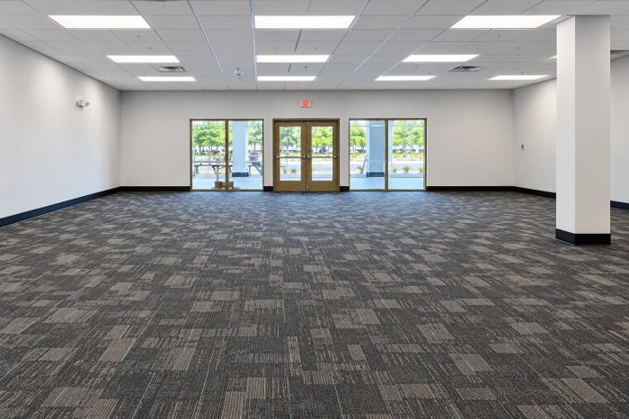 Open retail sales floor finished in patterned grey and tan carpet tile, with a structural column and glazed entry doors
