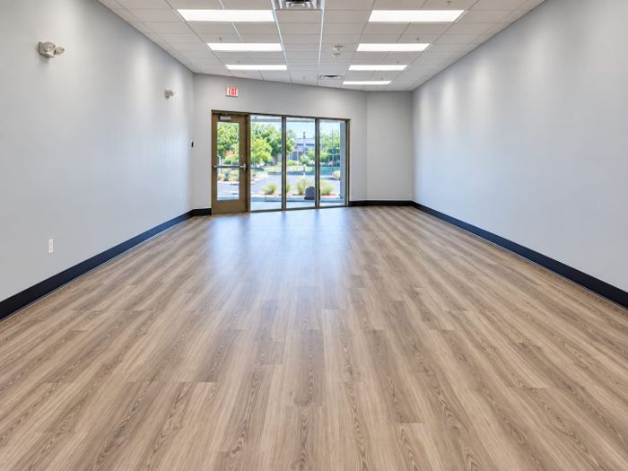 Bookstore side room with wood-look plank flooring and black vinyl wall base leading to a glazed exterior door
